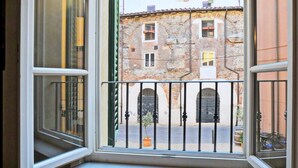 A room with an open window overlooking a courtyard with stone buildings and a metal gate. - Apartment in Lucca Near Amphitheater Square (Lucca)