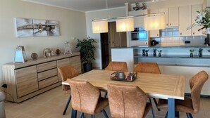 Eine moderne Küche mit einer zentralen Kochinsel, Pendelleuchten und einem Essbereich mit Holztisch und Ledersesseln.
