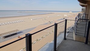 Ein Balkon mit Blick auf einen Strand, einen Steg und einen Rettungsschwimmturm.