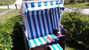 A beach chair with a striped cover, a cushion, and a small table with a drink and a book. - Just Before the Cape, Holiday Home B (Putgarten)