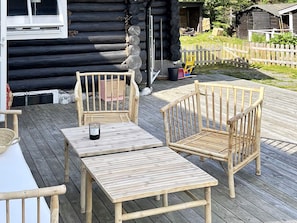 A wooden deck with a table and two chairs, a candle on the table, and a log cabin in the background. - 4 Star Holiday Home in Vintrosa (Vintrosa)