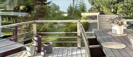 Une terrasse en bois offrant une vue sur un lac, avec des meubles d’extérieur et des plantes en pot.