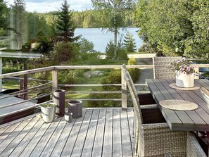 Um deck de madeira com vista para um lago, móveis de jardim e plantas em vasos.
