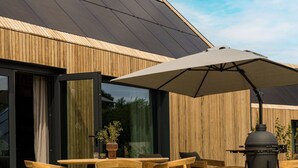 En udendørs terrasse med træmøbler, grill og stor parasol.