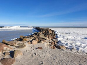 Une côte rocheuse avec une digue qui s’avance dans l’eau, sous un ciel bleu dégagé.