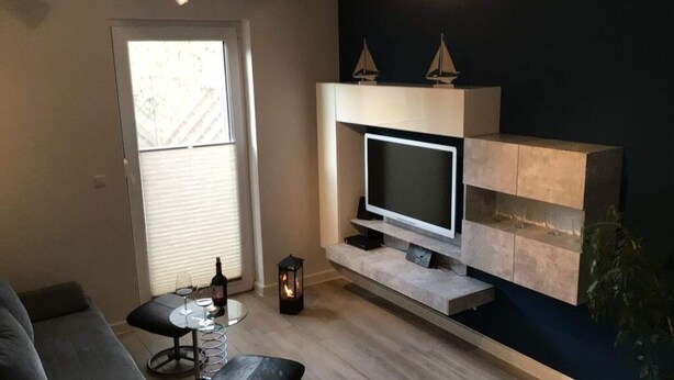 Ein modernes Wohnzimmer mit Flachbildfernseher, einer Couch, einem Couchtisch und einem kleinen Tisch mit Flasche und Gläsern.