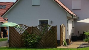 Ein zweigeschossiges Haus mit rotem Ziegeldach, einem hölzernen Tor und einem kleinen Garten.