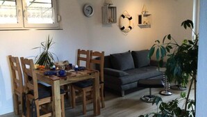 Ein Essbereich mit einem Holztisch und Stühlen, einem dunkelgrauen Sofa und einer Topfpflanze.