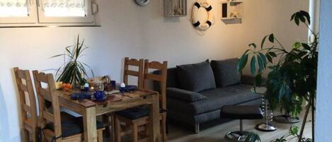 A dining area with a wooden table and chairs, a dark grey sofa, and a potted plant.