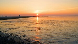 Een zonsondergang boven een rustig wateroppervlak, met een verre oever en windturbines.