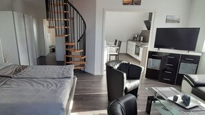 Een modern appartement met een bed, een zwarte leren bank, een eethoek, een keuken en een televisie.