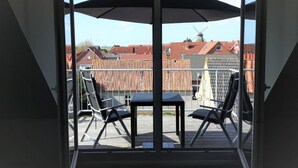 Een balkon met een tafel en stoelen, een windmolen op de achtergrond en gebouwen met rode daken.