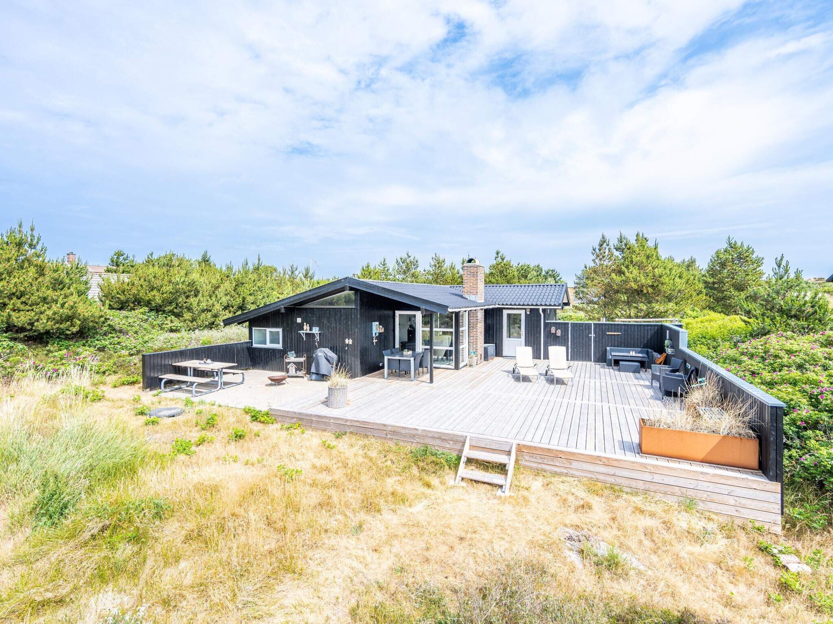 A modern house with a deck, outdoor seating, and a view of the surrounding landscape.