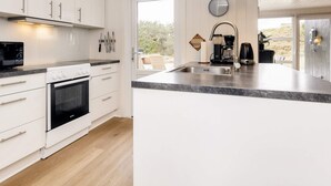 A modern kitchen with white cabinetry, a built-in oven, a large island with a sink, and a pendant light. - 4 Star Holiday Home in Henne (Henne)