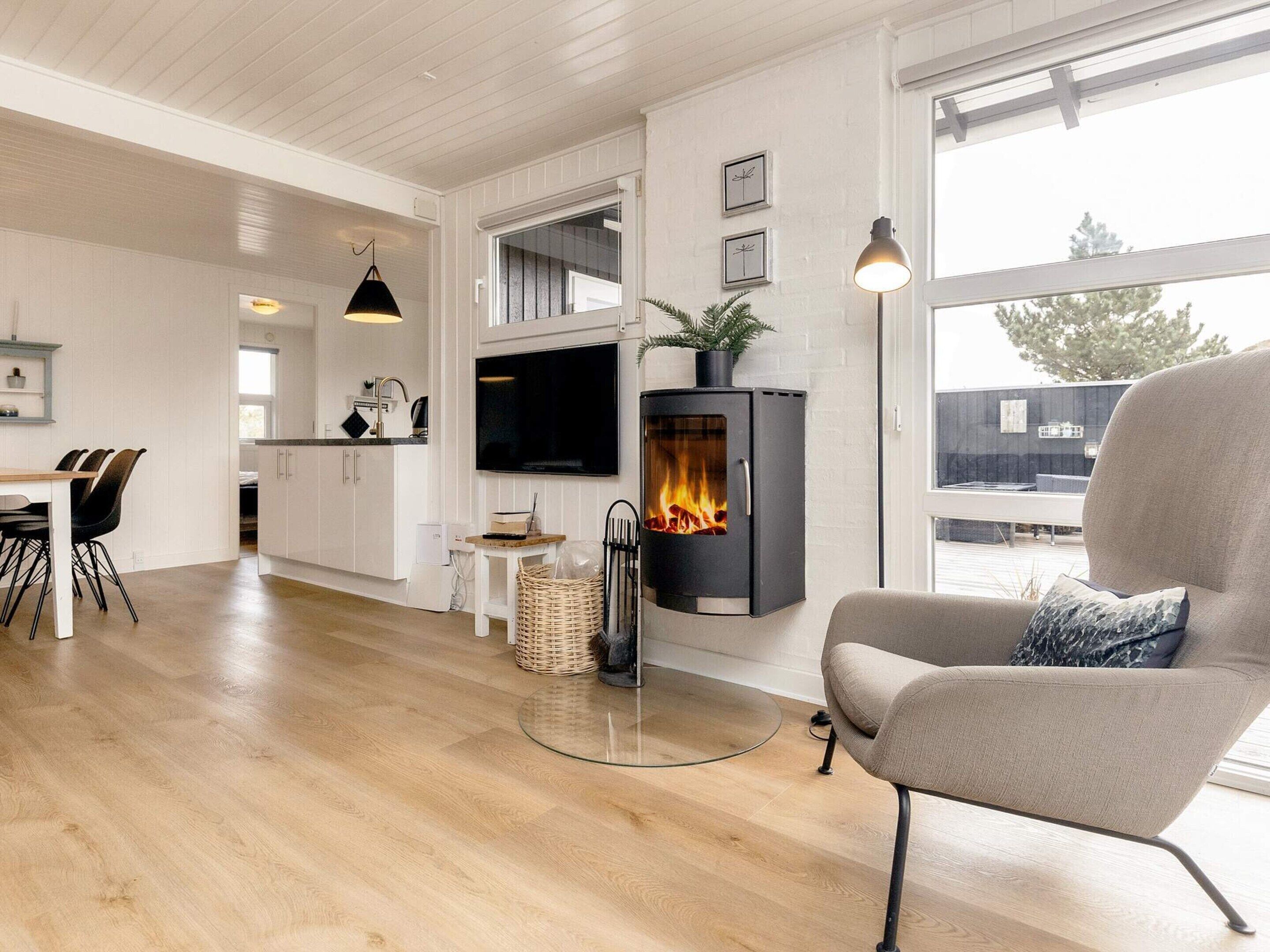 A modern living room with a fireplace, a dining area with chairs, and a kitchen with white cabinetry.