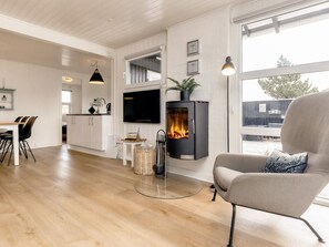 A modern living room with a fireplace, a dining area with chairs, and a kitchen with white cabinetry. - 4 Star Holiday Home in Henne (Henne)