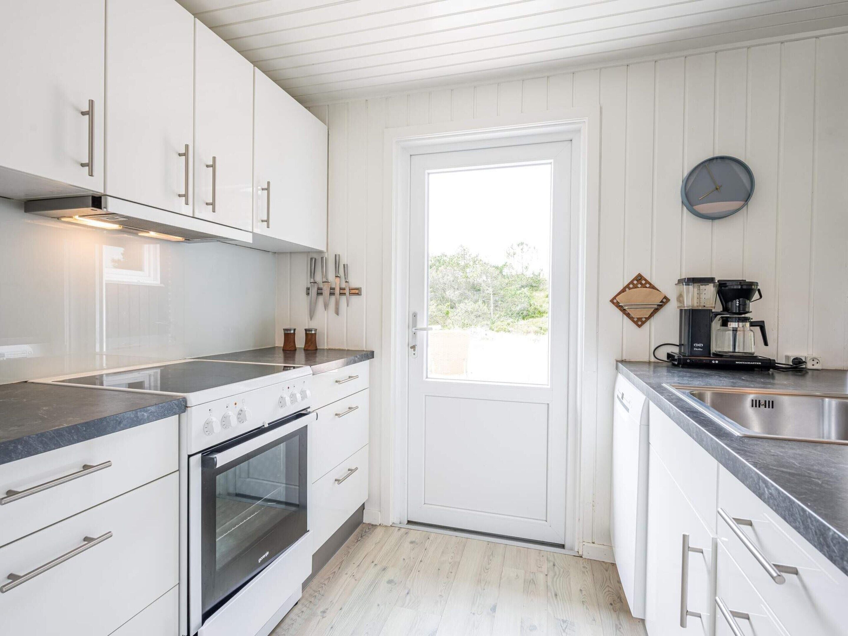 A kitchen with white cabinets, a built-in oven, a coffee maker, and a window with a view of greenery.