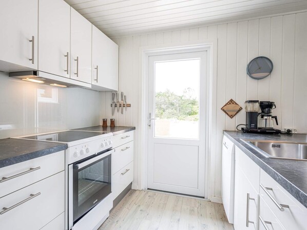 A kitchen with white cabinets, a built-in oven, a coffee maker, and a window with a view of greenery.