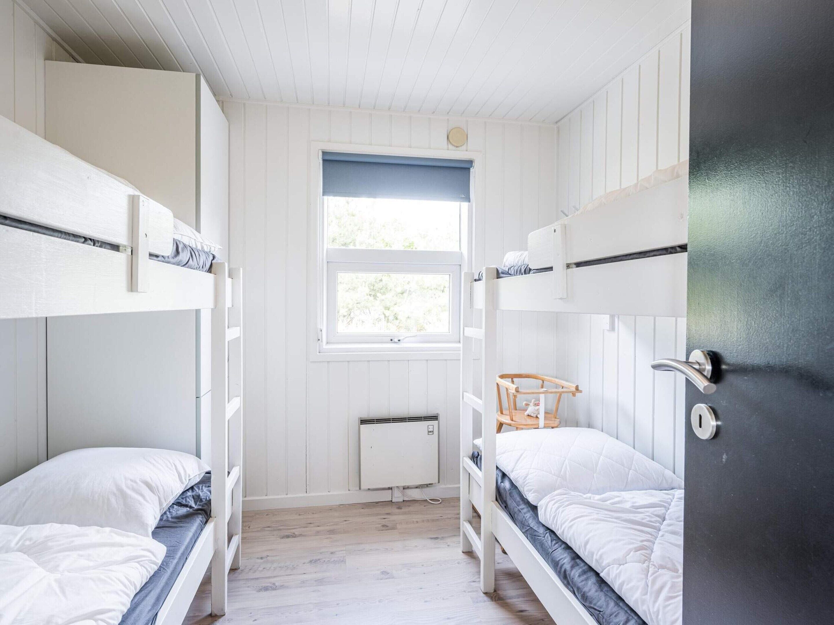 A bunk bed room with white walls, a window, and a radiator.