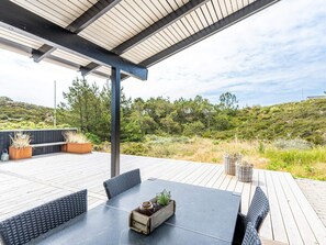 An outdoor patio with a table and chairs, surrounded by wooden decking and a view of a hilly landscape. - 4 Star Holiday Home in Henne (Henne)