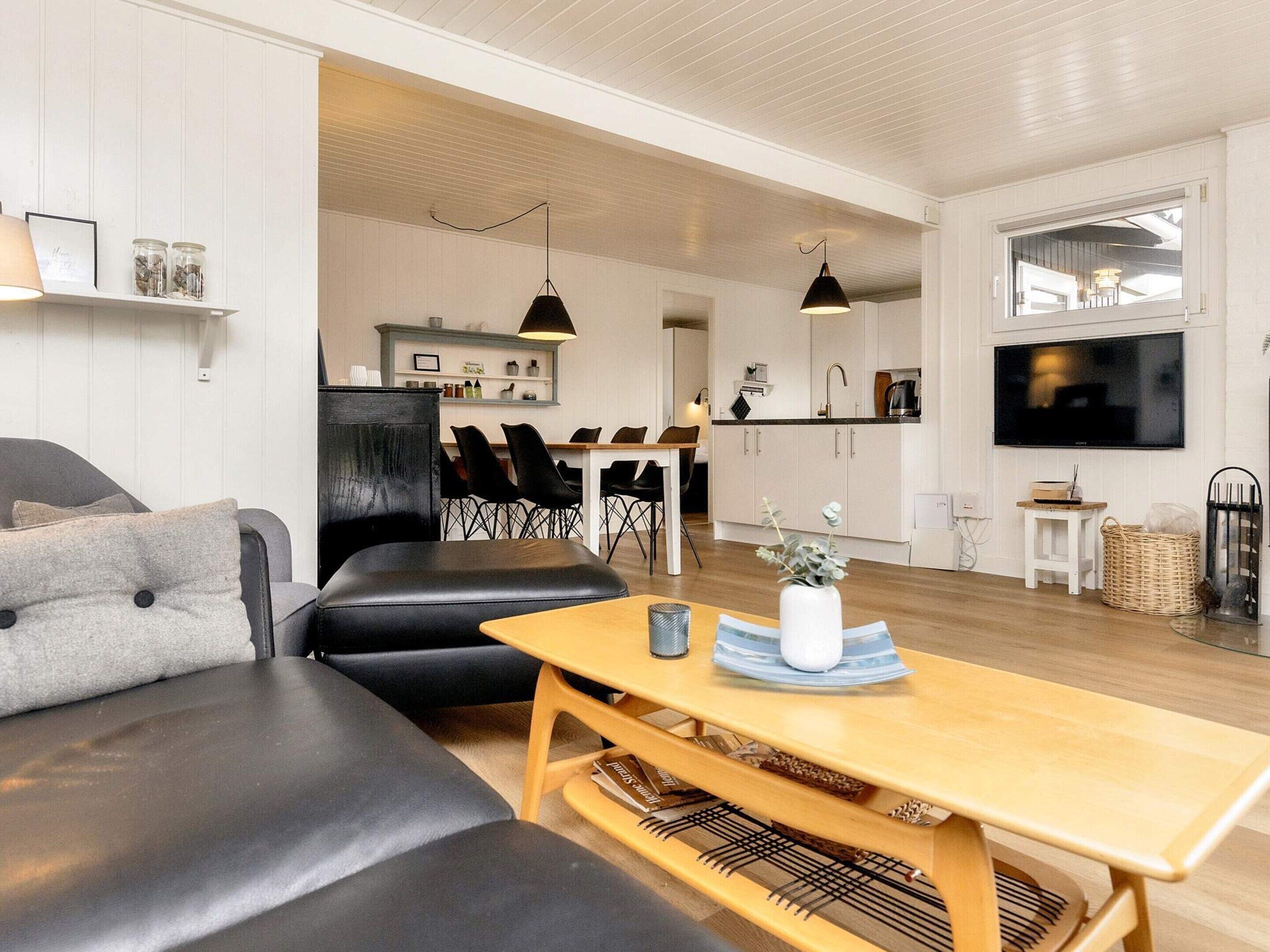 En moderne stue med sofa, sofabord i træ og spiseområde med stole.