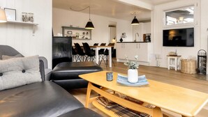 A modern living room with a sofa, a wooden coffee table, and a dining area with chairs. - 4 Star Holiday Home in Henne (Henne)