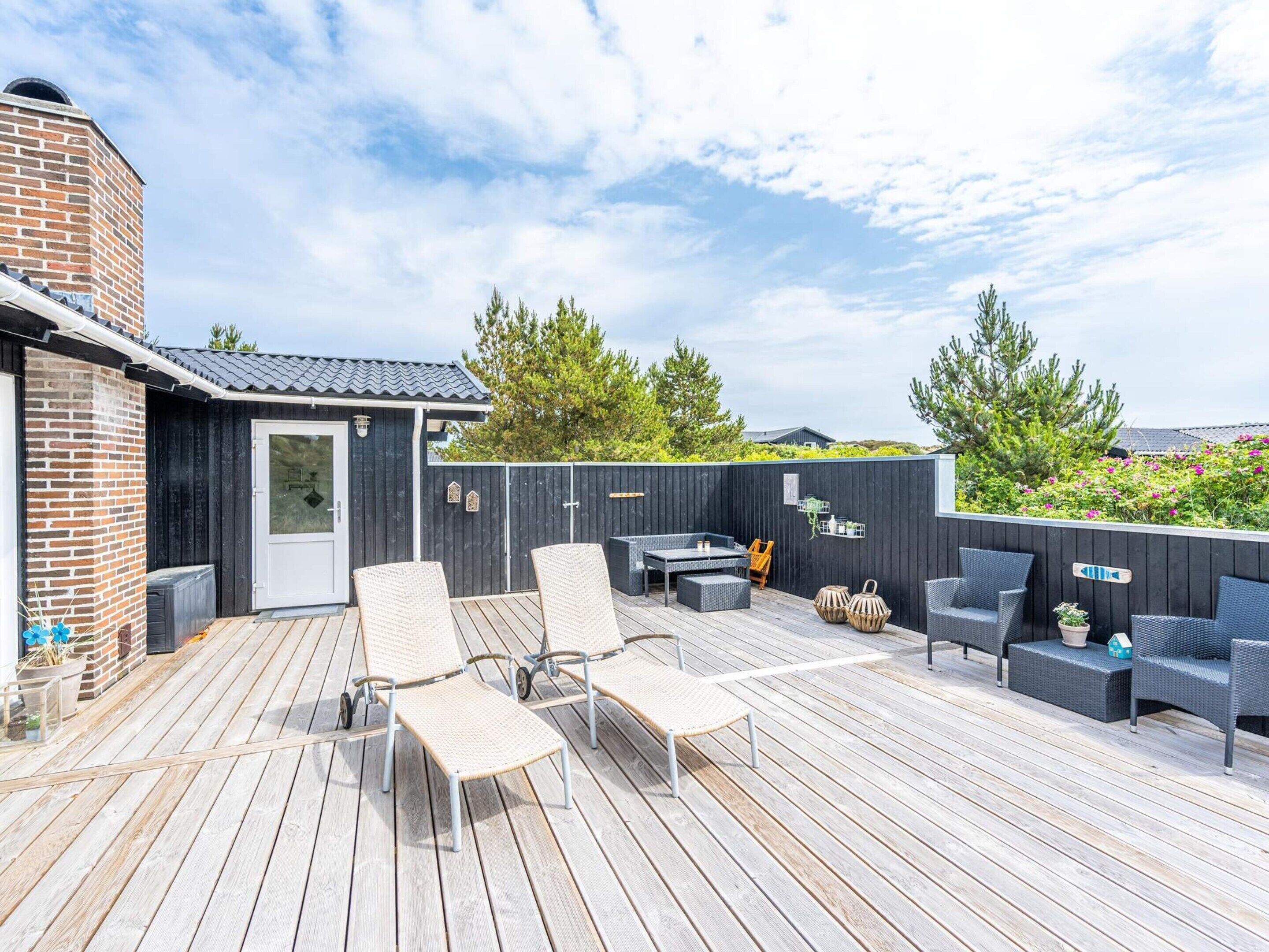 A wooden deck with outdoor furniture, a brick building, and a black fence.