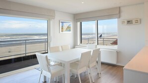 Una camera moderna con un'ampia finestra vista spiaggia, un tavolo da pranzo bianco e arredamento minimalista.