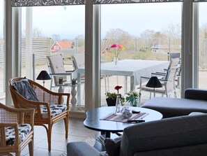 A room with a dining area, a sofa, and a view through large windows.