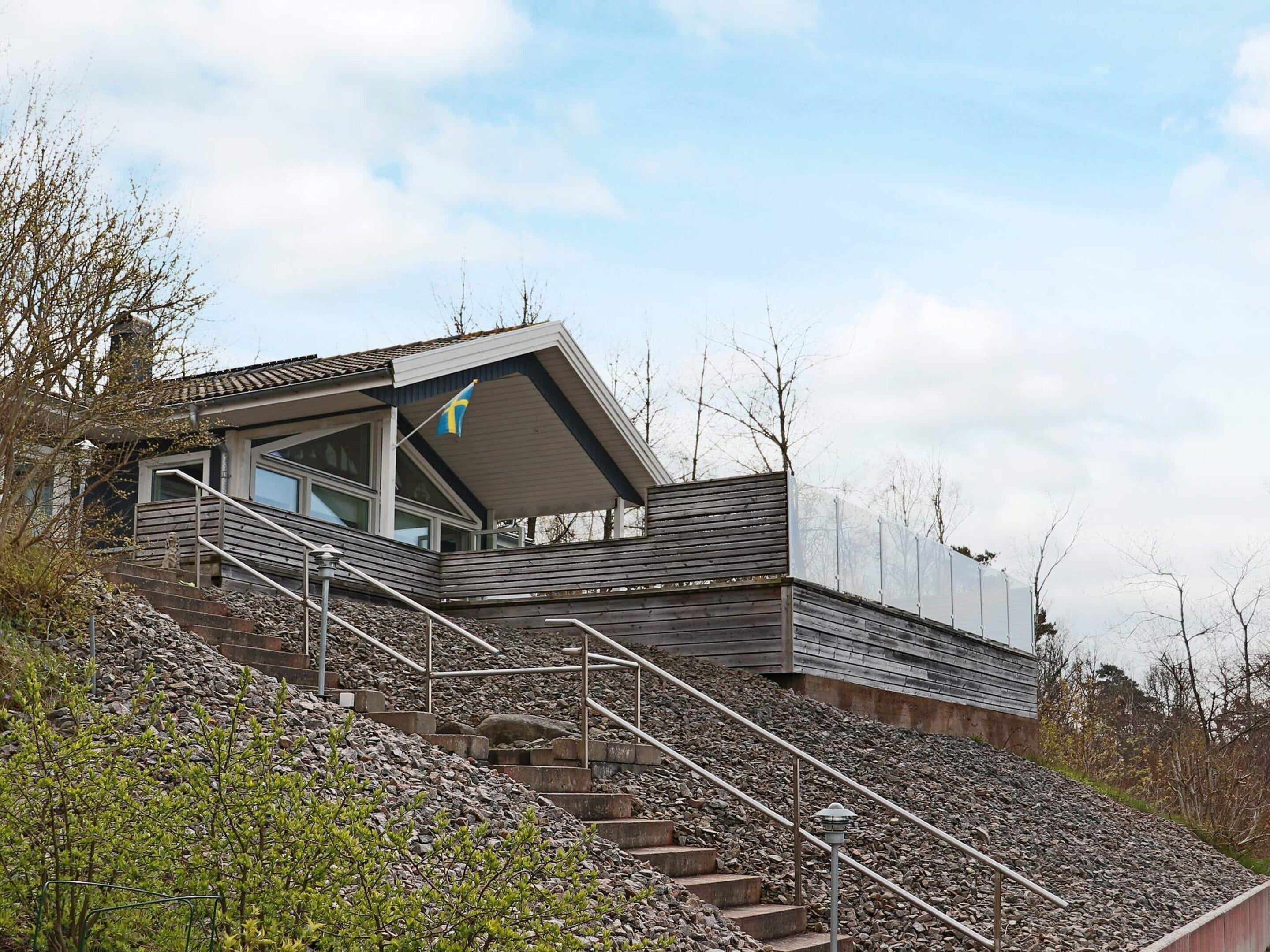 Uma casa moderna com telhado inclinado, uma escada que leva a um deck de madeira e uma bandeira no telhado.