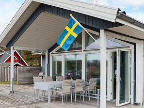 A modern building with a covered patio area featuring a table and chairs. - 5 Star Holiday Home in Steninge (Steninge)