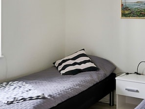 A single bed with a striped pillow, a bedside table with a power cable, and a wall-mounted picture.