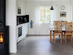 A modern kitchen with a wood-burning stove, white cabinets, and a dining area with wooden chairs.
