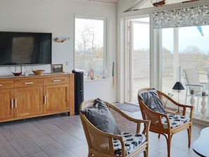 A room with a television, wooden cabinets, wicker chairs, and a large window.