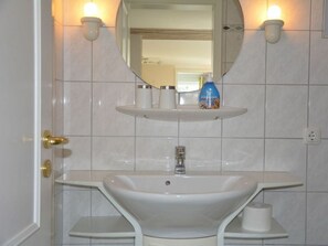 A bathroom with a white sink, a mirror, and two wall-mounted lights. - "beach Bunny" in the House on the Dune (Wittduen)