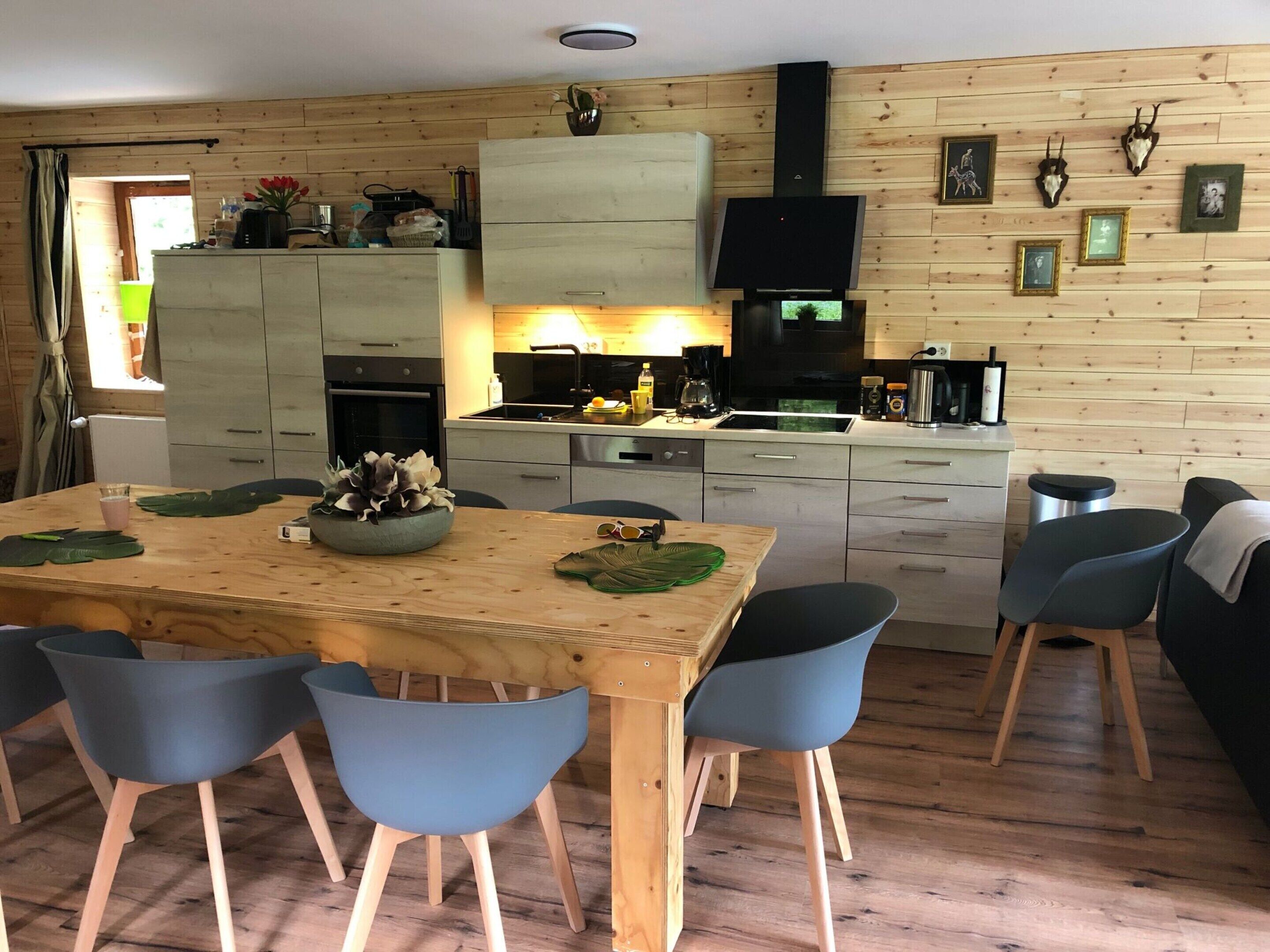 A modern kitchen with wooden cabinets, a central island, and a dining area with blue chairs.
