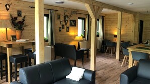 Un interior de cabaña acogedor, con paredes de madera, un sofá de cuero negro, comedor y cocina.