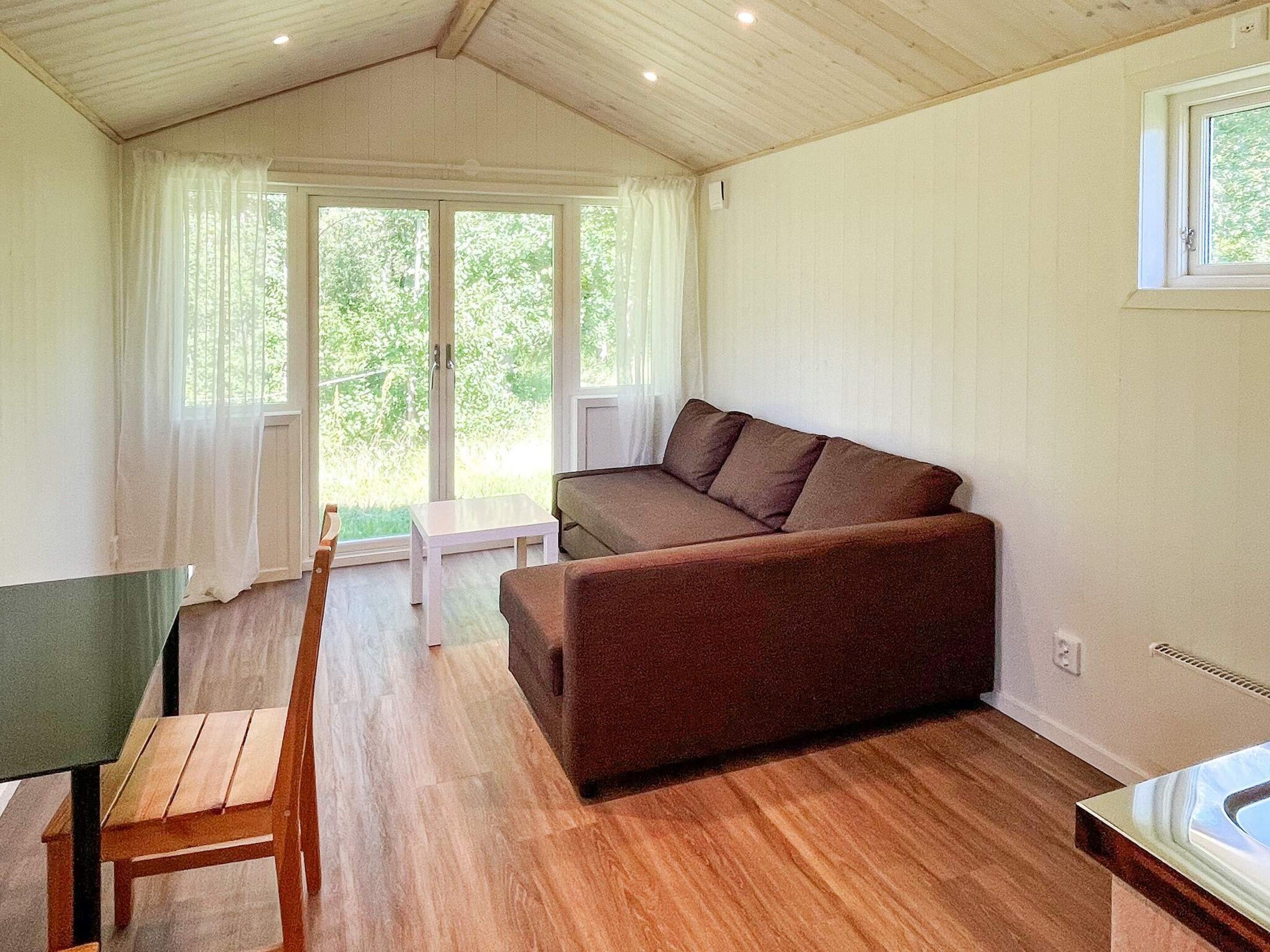 A room with a wooden floor, a brown sofa, a small white table, and a wooden chair.