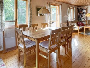 A wooden dining table with chairs, a bookshelf, and a lamp in a room with wooden floors and large windows. - 7 Person Holiday Home in Rockneby (Rockneby)