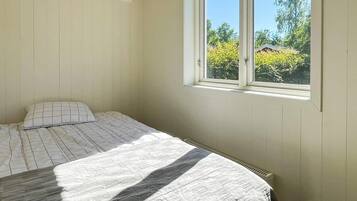 A bedroom with a single bed, a window with a view of greenery, and a wall-mounted air conditioning unit.