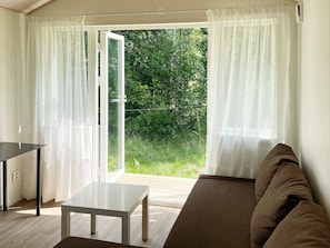 Una habitación con puerta de vidrio corrediza que da a un jardín, una mesa blanca y un sofá marrón.