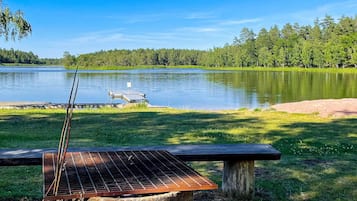 A picnic area with a grill and a bench overlooking a lake.