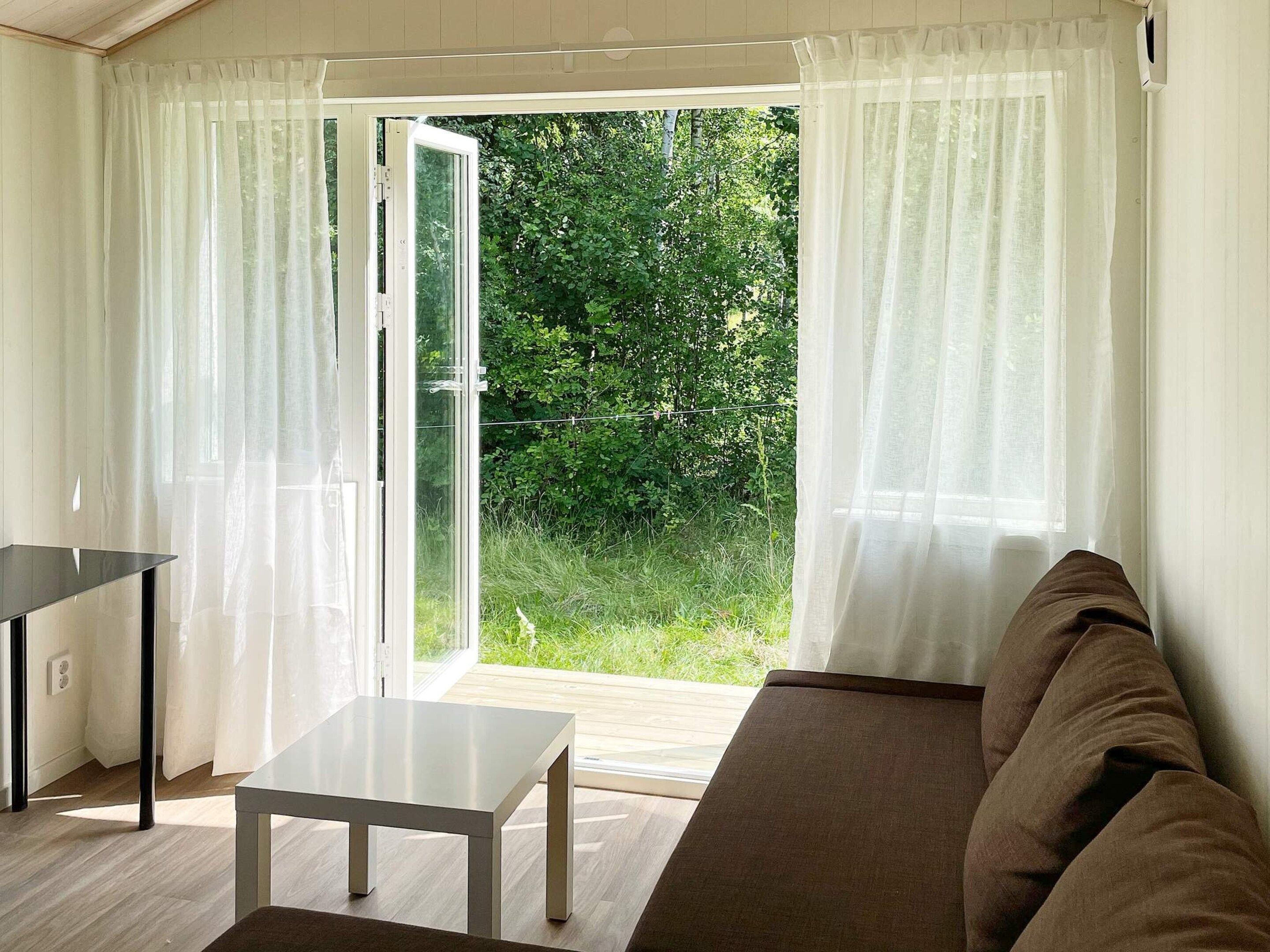 A room with a sliding glass door leading to a garden, a white table, and a brown sofa.