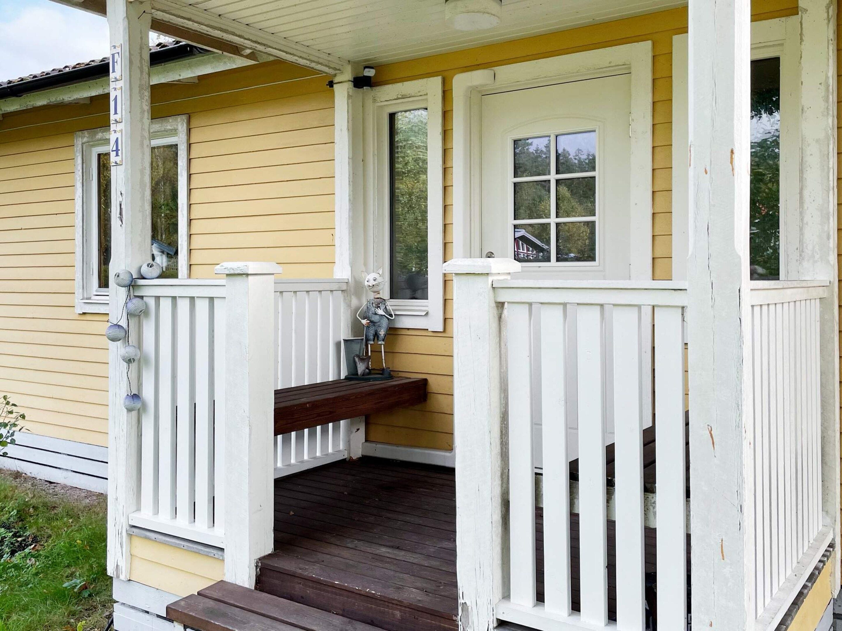 A yellow house with a porch, white railings, and a wooden bench.