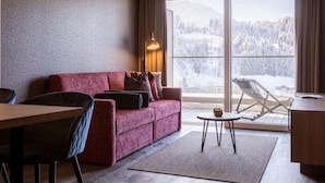 Ein modernes Wohnzimmer mit einem roten Sofa, einem Esstisch und Blick auf eine verschneite Landschaft durch große Fenster.