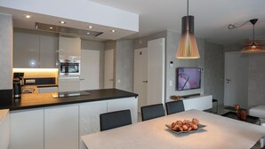 Et moderne køkken med en central ø, et spiseområde med bord og stole, og et tv ophængt på væggen.