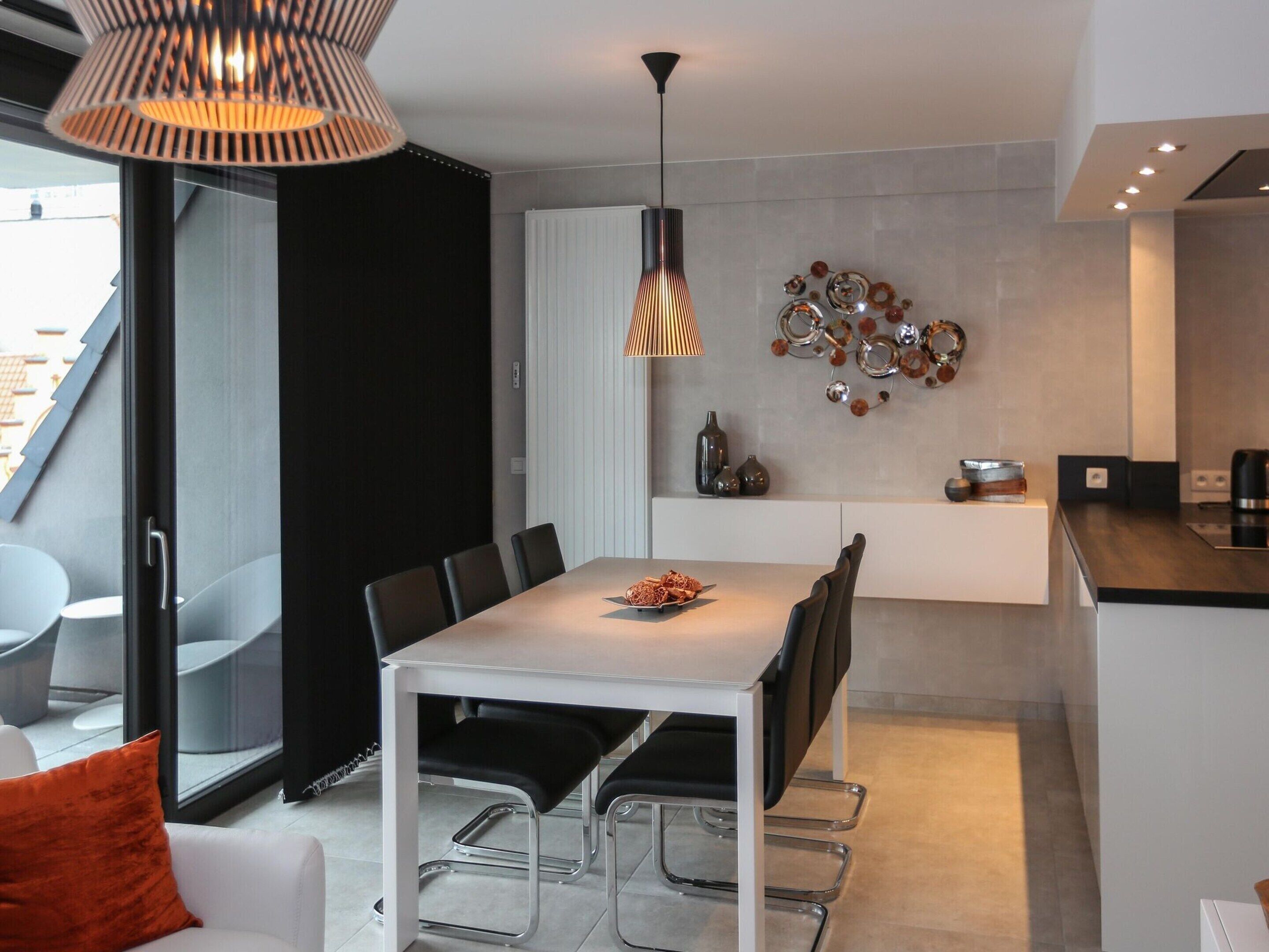 Une cuisine moderne avec un coin repas, comprenant une table blanche, des chaises noires et un luminaire suspendu original.