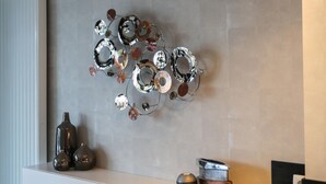 Et moderne interiør med en vægmonteret metalskulptur, et hvidt konsolbord med dekorative genstande, og en sort bordplade.