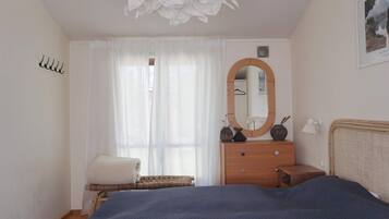 A bedroom with a bed, a dresser, a mirror, a clock, and a window with curtains.