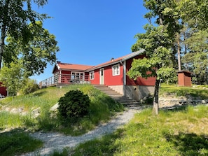 A red wooden house with a porch and a staircase leading to the entrance. - 4 Star Holiday Home in Akersberga (Akersberga)